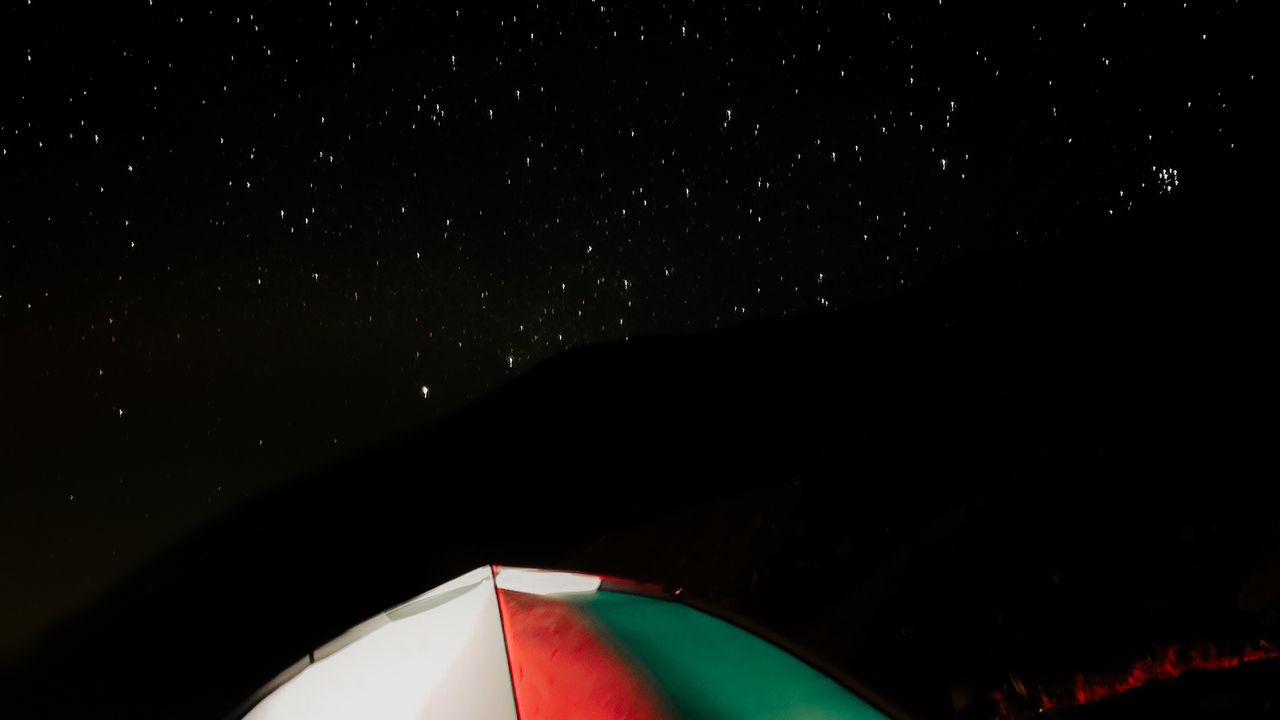 Barraca iluminada sob céu estrelado em acampamento selvagem