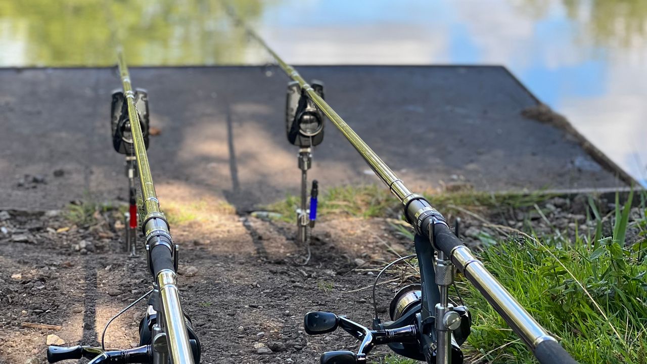 Duas varas de pesca montadas à beira de um lago, prontas para receber os alarmes de fisgada