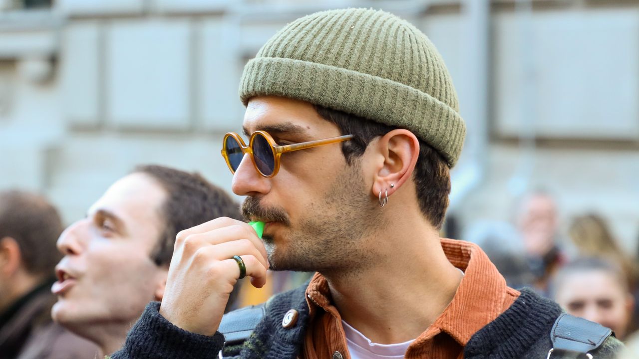 Homem de gorro e óculos escuros usando um apito ao ar livre