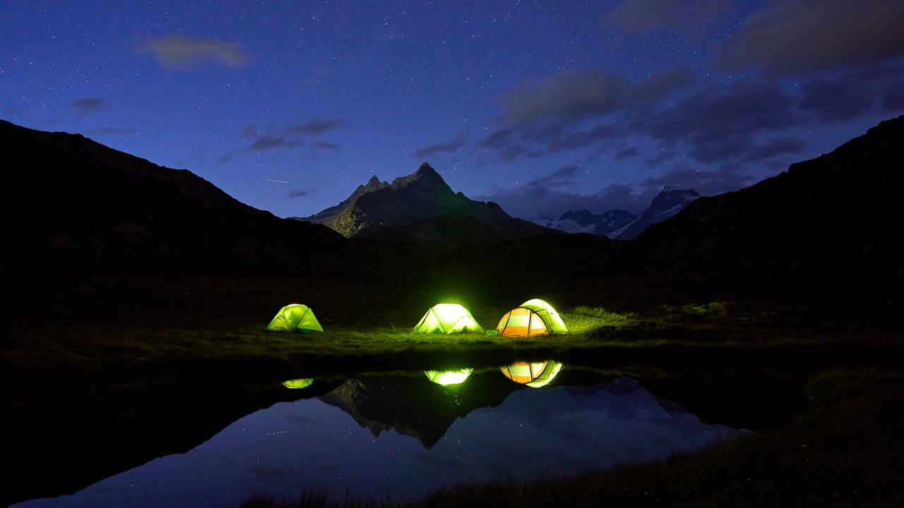 Barracas de camping montadas à beira de um lago de montanha sob céu estrelado