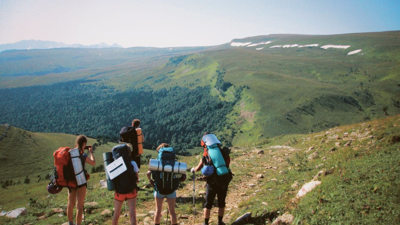 Grupo de amigos com mochilas caminhando em trilha de montanha para acampar