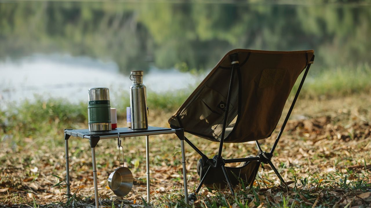 Cadeira dobrável de camping montada às margens de um rio em área de acampamento