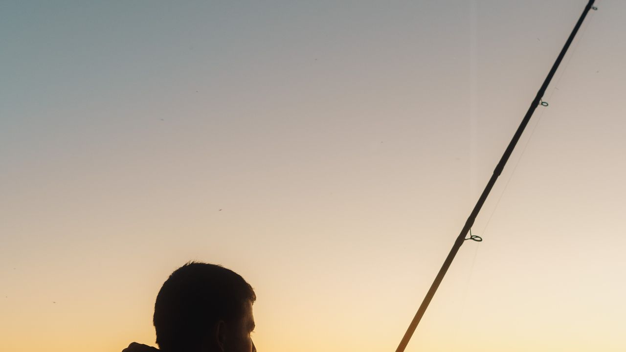 Pescador ao entardecer usando proteção solar na beira do rio