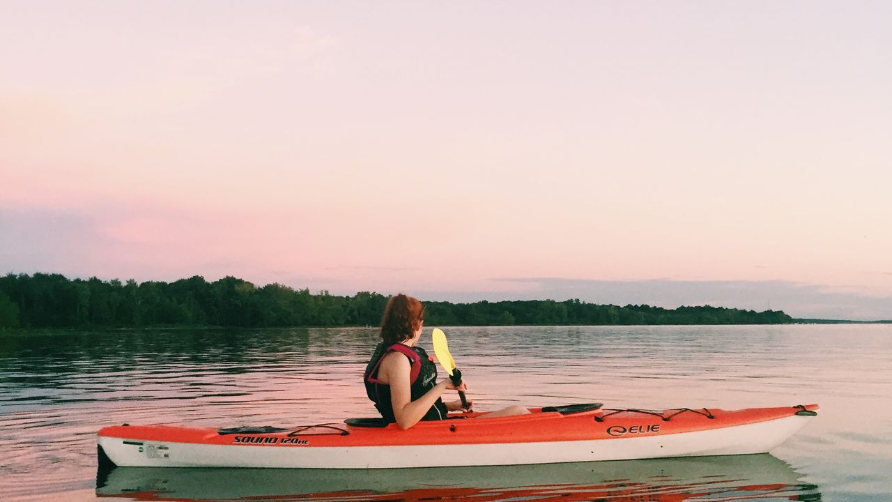 Pessoa remando de caiaque em lago calmo usando colete de flutuação
