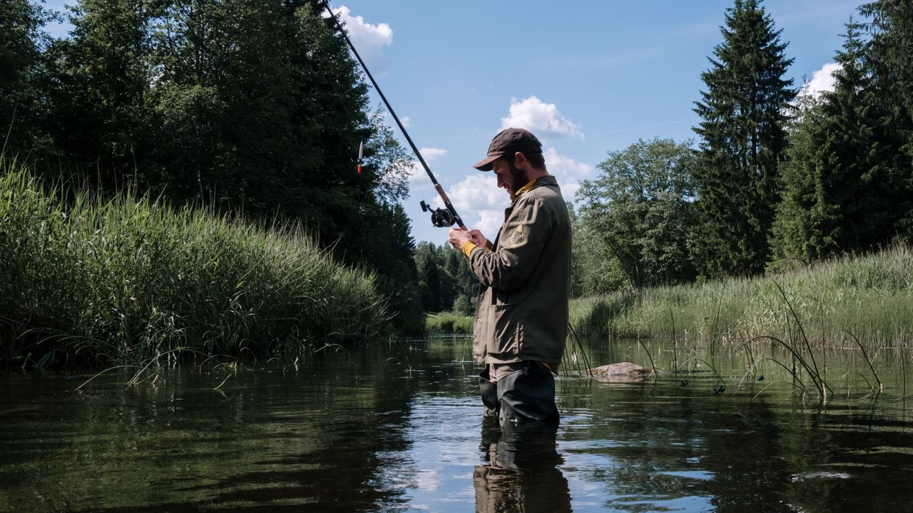 Pescador de colete às margens de um rio cercado de mata