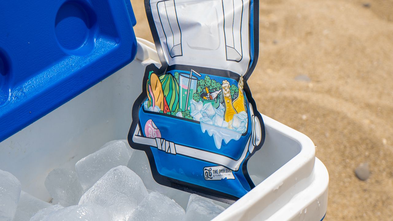 Cooler azul aberto na areia da praia com gelo e bebidas