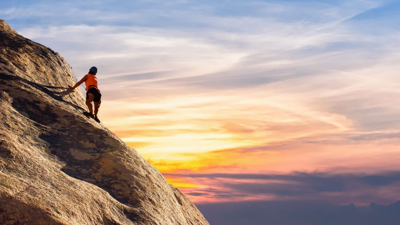Praticante de escalada descendo uma parede de rocha ao pôr do sol