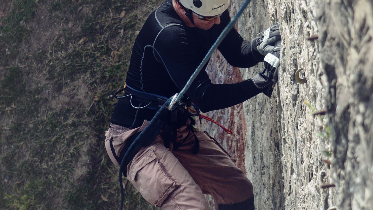 Pessoa escalando uma rocha com capacete e equipamento de segurança