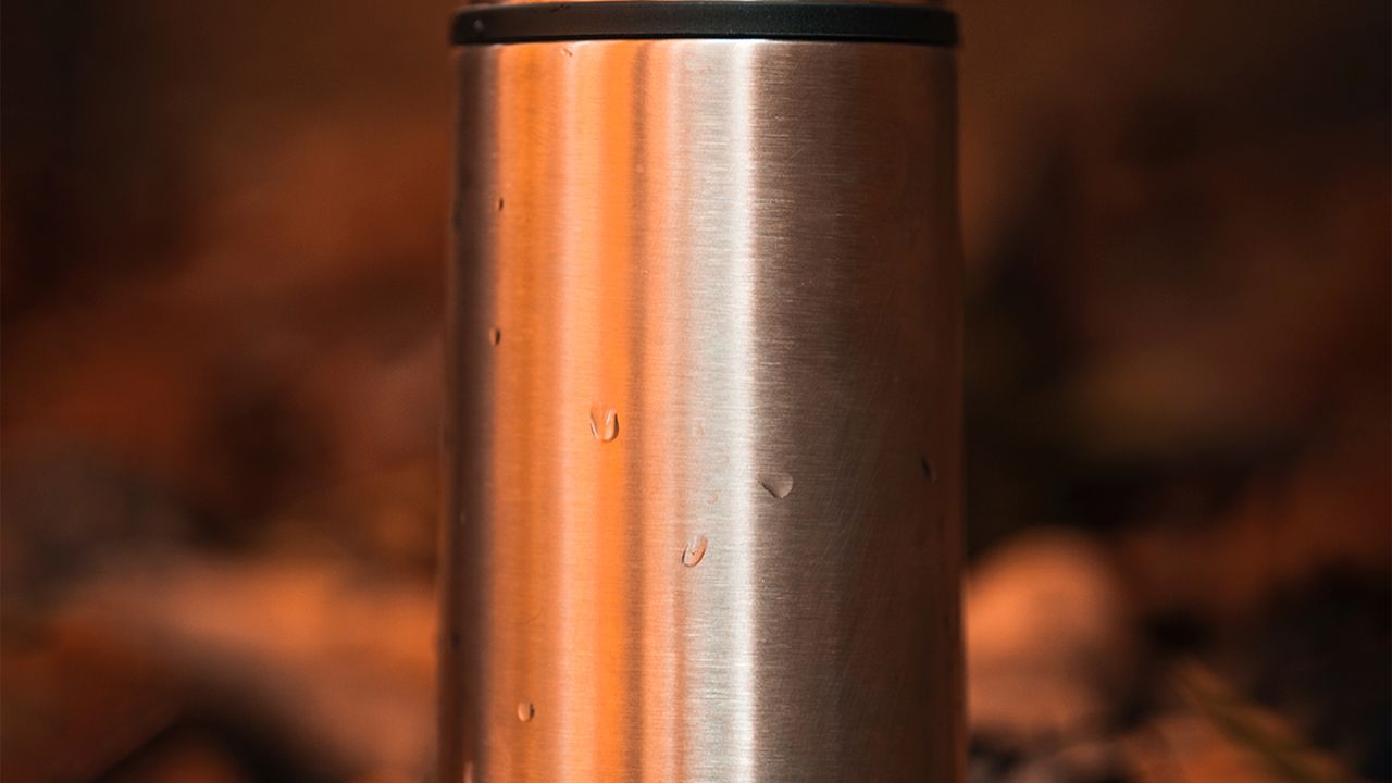 Garrafa térmica de aço inox apoiada ao ar livre em meio à natureza
