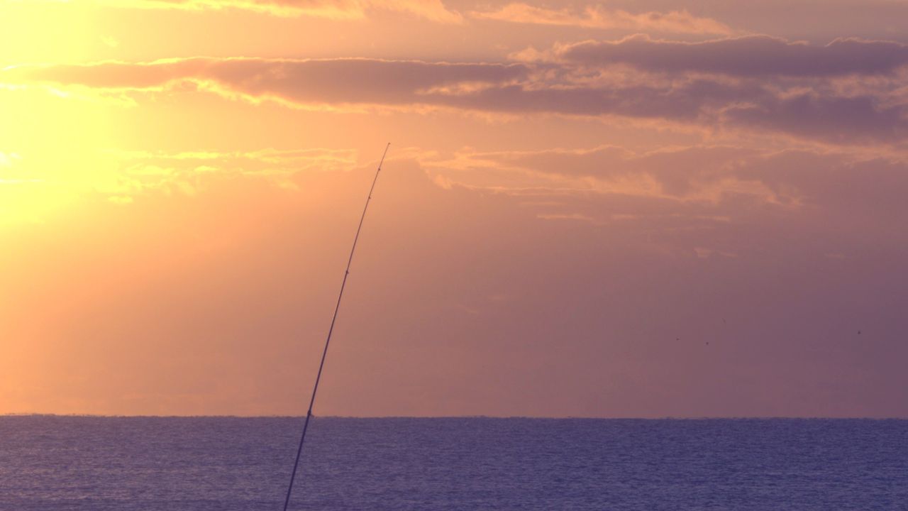 Pessoa pescando na praia com vara e isca artificial ao pôr do sol