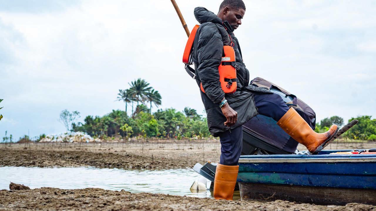 Pescador de botas impermeáveis descendo de um barco em margem lamacenta de mangue
