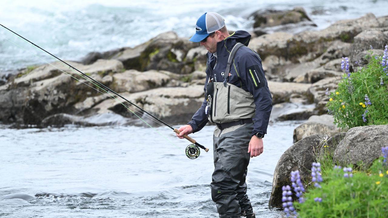 Pescador com botas de vadeio dentro de um rio durante a pescaria
