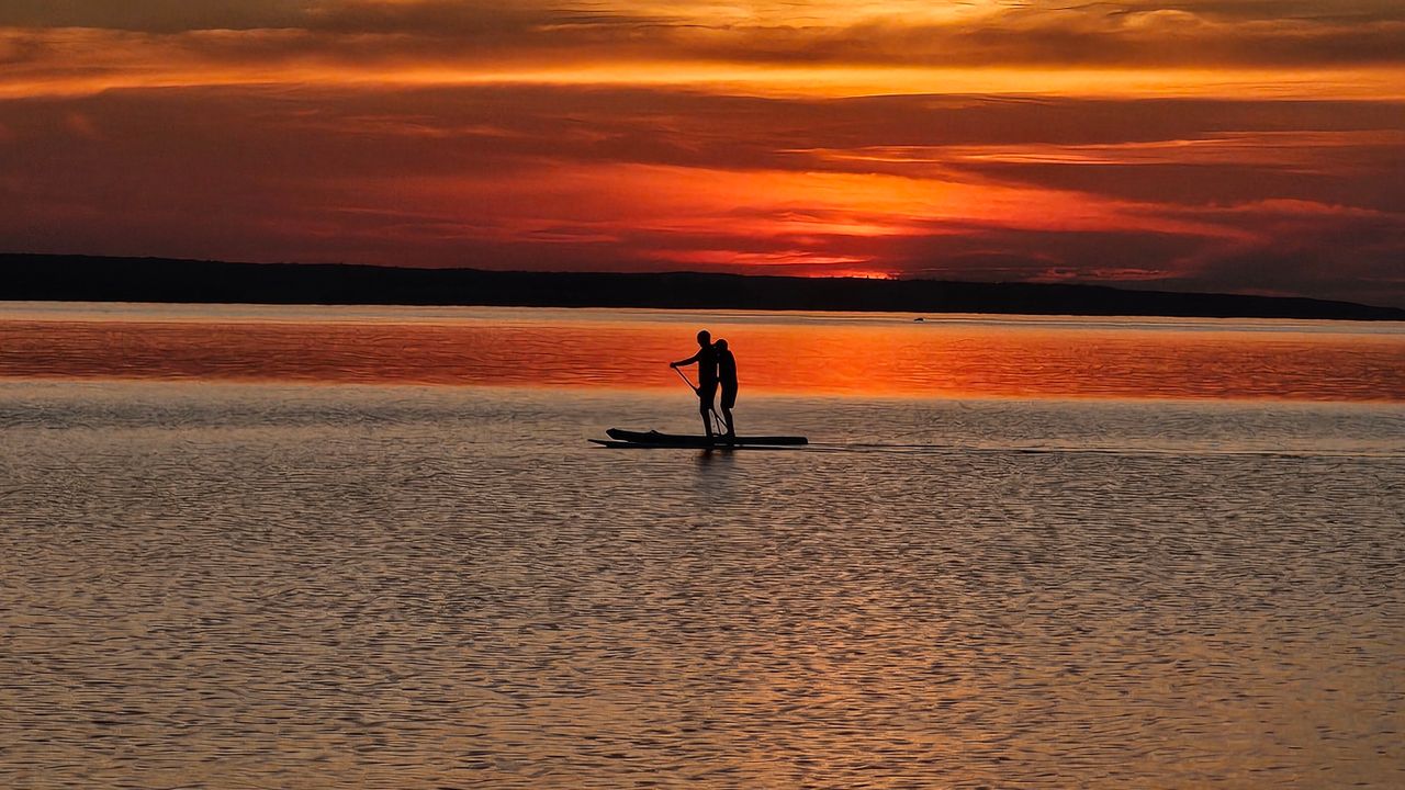 Pessoa remando em pé em prancha de stand up paddle em água calma